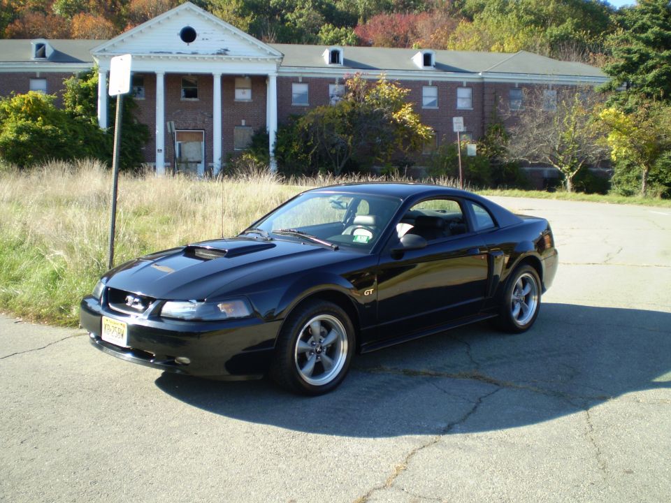 Black 2002 Ford Mustang GT parked in front of an abandoned building.