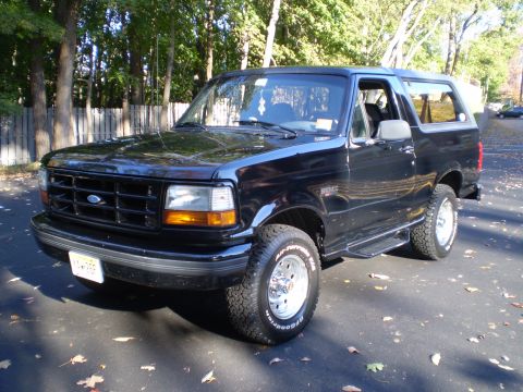 1996 Ford Bronco - A black 1996 Ford Bronco is parked on an asphalt driveway with fallen leaves scattered around. The front passenger side of the SUV is visib…