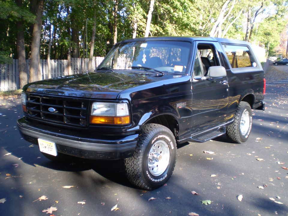 Black 1996 Ford Bronco parked on driveway with fallen leaves.