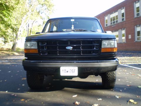 1996 Ford Bronco - Front view of a black Ford Bronco parked on an asphalt surface with fallen leaves. The vehicle has a black grille with a Ford logo and a li…