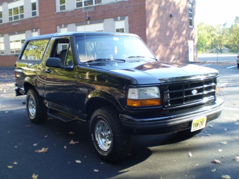 1996 Ford Bronco - A black 1996 Ford Bronco is parked in front of a brick building. The front 3/4 view shows the vehicle's grille, headlights, and front bumpe…