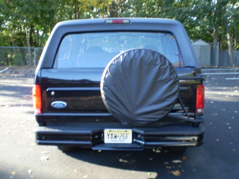 1996 Ford Bronco - The rear of a black Ford Bronco is shown parked outdoors on an asphalt surface, with a spare tire mounted on the back. A New Jersey license…