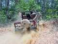 1985 Ford Bronco - An off-road vehicle navigates a dusty trail surrounded by trees.