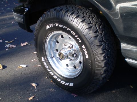 1996 Ford Bronco - A close-up view of a BFGoodrich All-Terrain T/A tire on a chrome wheel, mounted on a black Ford Bronco. Fallen leaves are scattered on the…