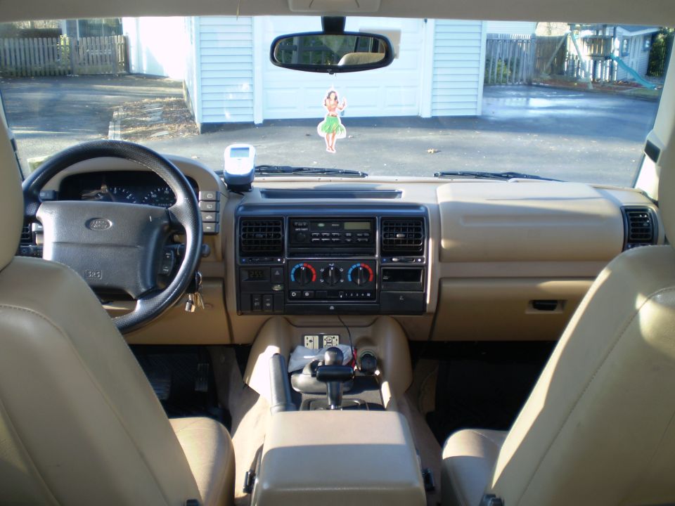 Interior of a 1996 Land Rover Discovery, showing dashboard, steering wheel, center console, and hula dancer ornament.