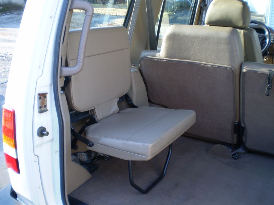 Interior of a tan SUV showing a folded rear jump seat.