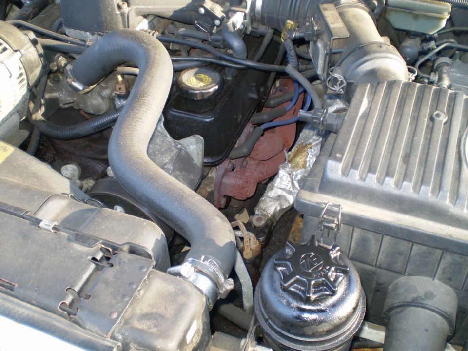 Engine bay with black radiator hose, reservoir cap and rusty manifold