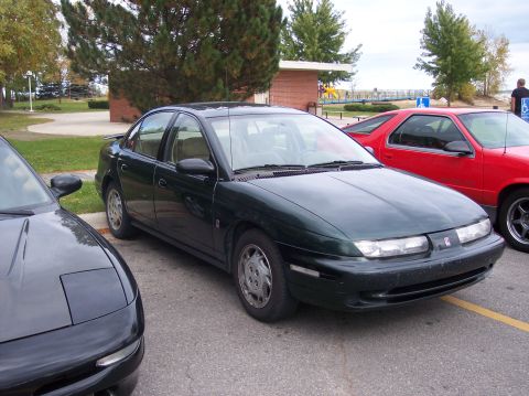 1996 Ford Probe - A dark green sedan is parked next to a black car and a red car in a parking lot. The dark green sedan is a Saturn, and the black car appear…