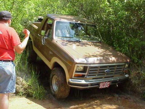 1985 Ford Bronco - A brown 1980s Ford Bronco navigates a muddy, wooded trail.