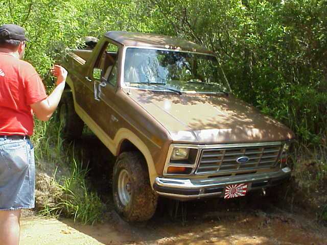 Brown 1980s Ford Bronco on a dirt trail, front 3/4 view