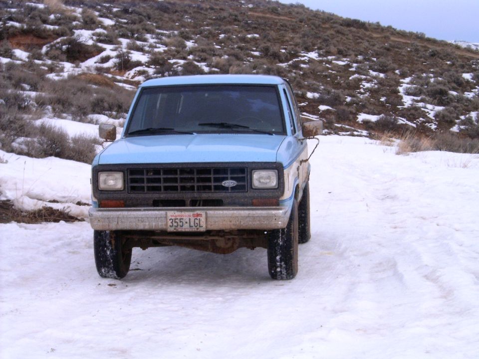 Light blue 1988 Ford Bronco parked in snow with a brushy hill in the background.