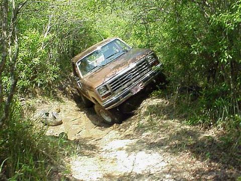 1985 Ford Bronco - Ford Bronco driving through mud and vegetation.