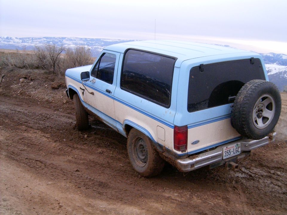 1988 Ford Bronco on a muddy trail with mountains in the background.