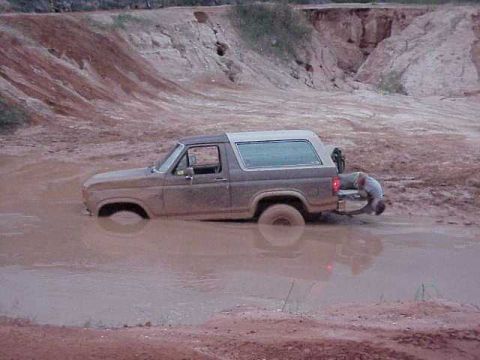 1985 Ford Bronco - A person attempts to free a Ford Bronco that is stuck deep in a muddy pit.
