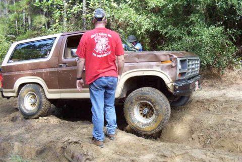 1985 Ford Bronco - A brown Ford Bronco navigates a challenging off-road course with one wheel stuck in a rut.