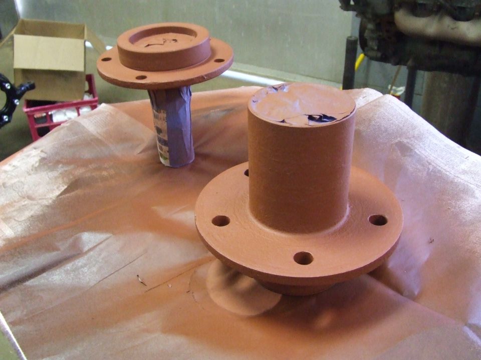 Two painted metal parts with flanges and cylindrical sections on brown paper.