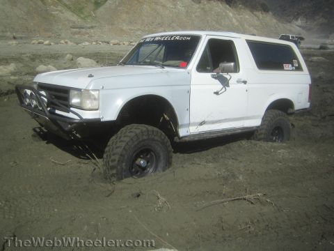 1990 Ford Bronco - Photo of a white lifted Ford Bronco in mud, not a technical document.