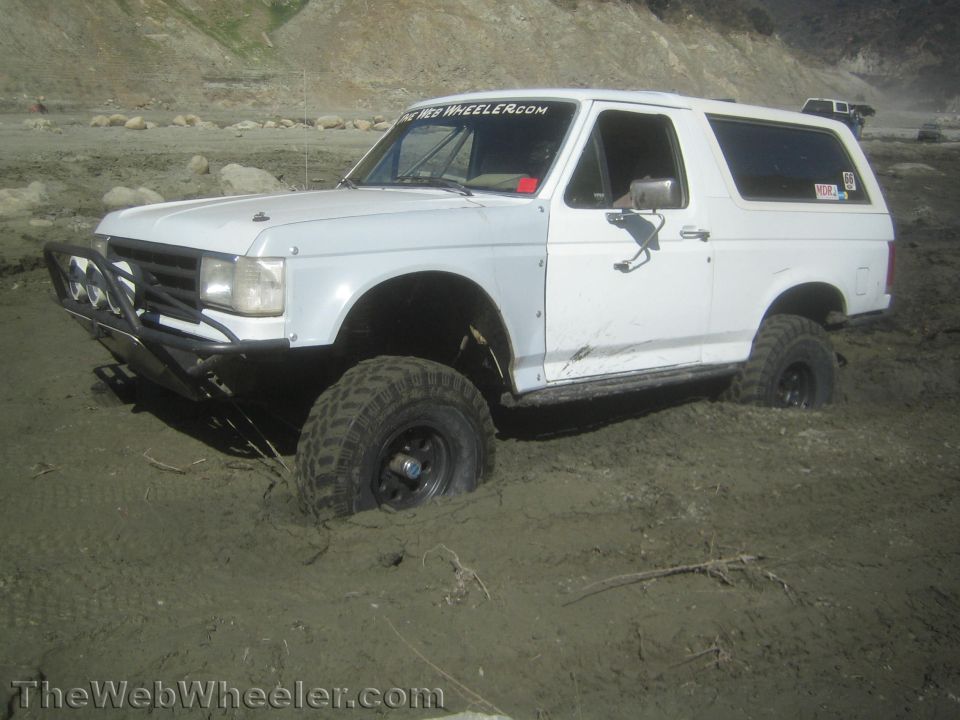White lifted Ford Bronco stuck in a muddy riverbed