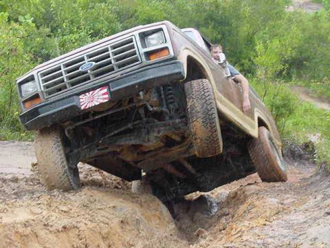 1985 Ford Bronco - A driver navigates a challenging muddy trail in a brown 1980s Ford Bronco.