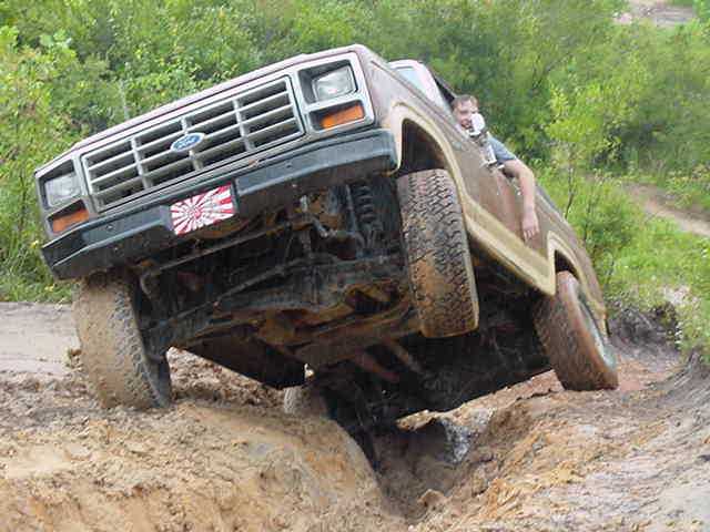 Brown 1980s Ford Bronco climbing a muddy off-road hill with door open
