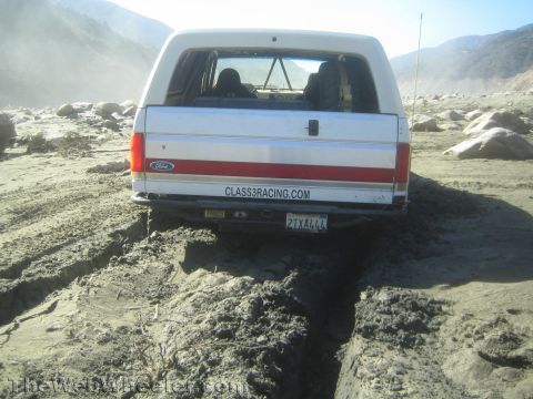1990 Ford Bronco - Photo of the rear of a white Ford Bronco stuck in a muddy wash, not a technical document.