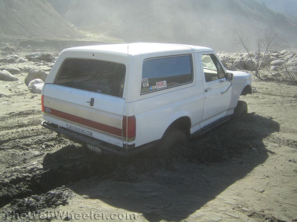 Side rear view of a white Ford Bronco stuck in mud
