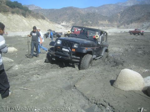 1990 Ford Bronco - Photo of a black Jeep Wrangler stuck in mud being recovered, not a technical document.