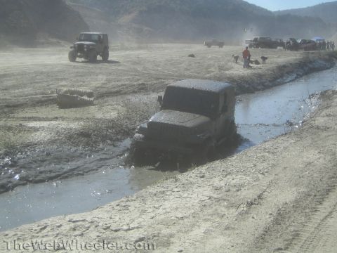1990 Ford Bronco - Photo of a muddy Jeep crossing a water trench off-road, not a technical document.