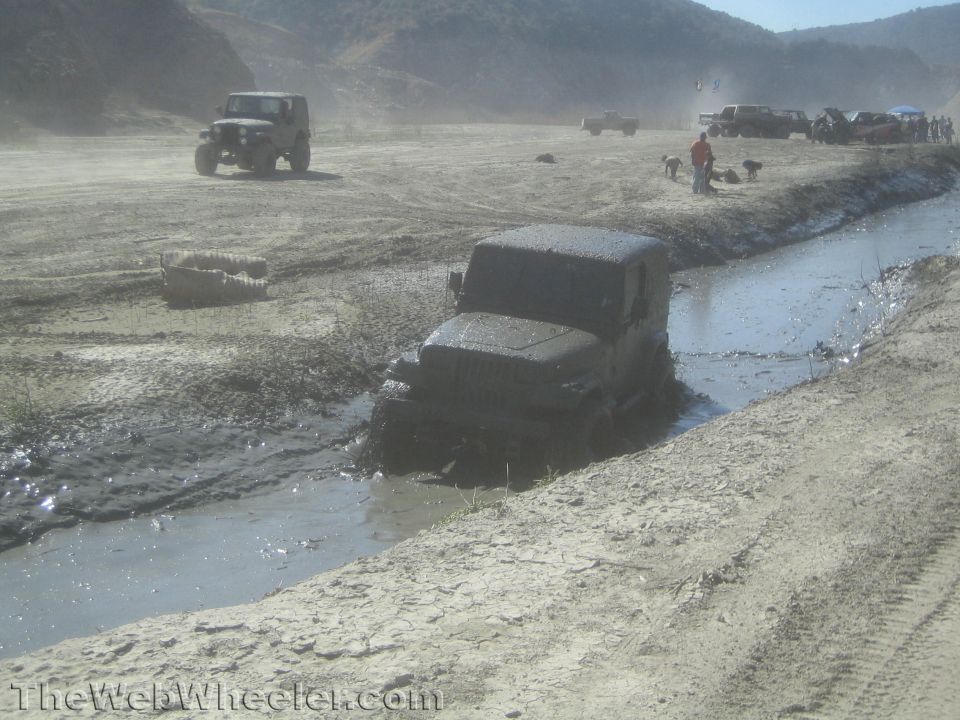 Muddy Jeep Wrangler driving through a water trench in a wash