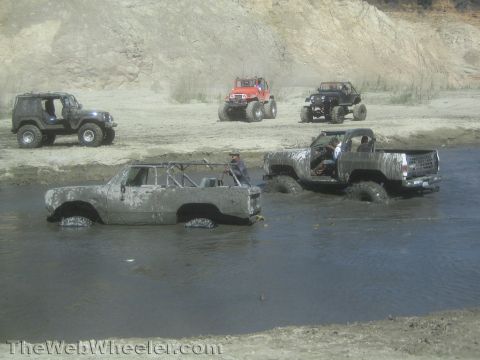 1990 Ford Bronco - Photo of multiple off-road vehicles crossing a muddy water hole, not a technical document.