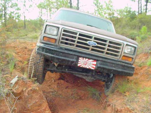 1985 Ford Bronco - Ford Bronco navigating a steep, muddy incline during an off-road excursion.