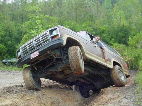 1985 Ford Bronco - This 1980s Ford Bronco is navigating a challenging off-road trail with steep inclines and muddy terrain.