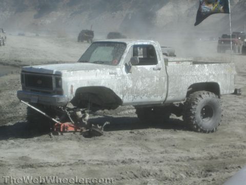 1990 Ford Bronco - Photo of a mud-coated Chevy pickup on a jack in sand, not a technical document.