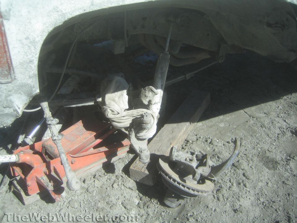 Vehicle parts, a floor jack and tools on the ground under a truck