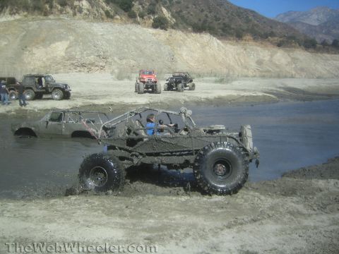 1990 Ford Bronco - Photo of a muddy tube-chassis buggy exiting a water hole, not a technical document.