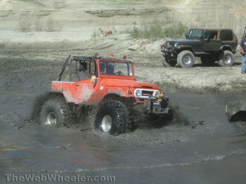 1990 Ford Bronco - Photo of an orange FJ40 Land Cruiser crossing a mud pit, not a technical document.