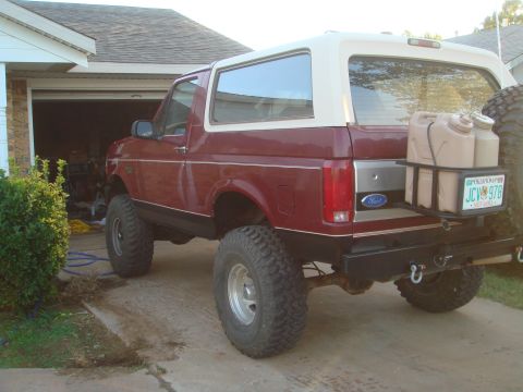 1992 Ford Bronco - The rear passenger side of a lifted, dark red 1992 Ford Bronco is parked in a driveway in front of an open garage. The Bronco has a white r…