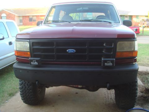 1992 Ford Bronco - Front view of a dark red Ford Bronco with a black grille and bumper. Two Baja Designs auxiliary lights are mounted on the front bumper.