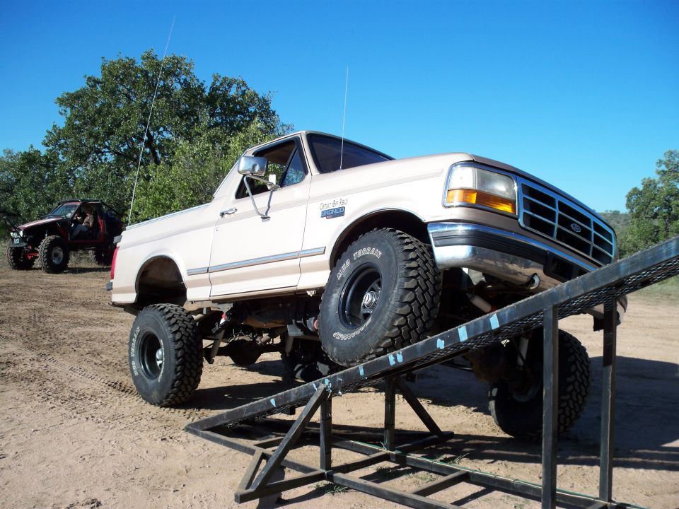 1996 Ford Bronco on a ramp, front tires elevated. Off-road vehicle in background.