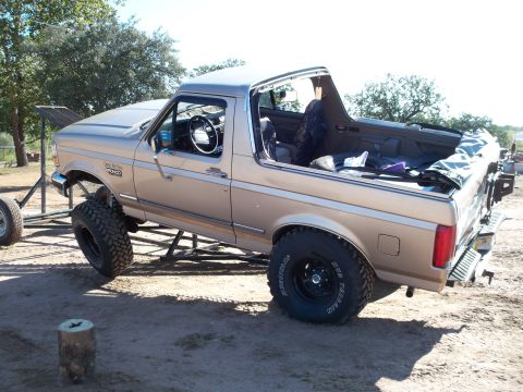 1996 Ford Bronco - Lifted two-tone tan/brown Ford Bronco with its removable rear hardtop lifted off and set behind the truck, shown from the driver-side rear…
