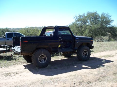 1996 Ford Bronco - Dark blue full-size Ford Bronco with the fiberglass rear top removed, shot from the passenger rear three-quarter angle on a dirt clearing w…