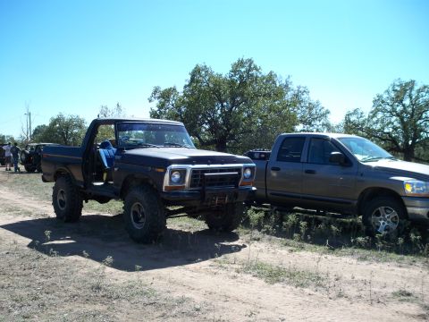 1996 Ford Bronco - A black square-body Ford 4x4 with its top and doors removed, blue interior visible, sits lifted on chunky mud tires with a front tube bumpe…