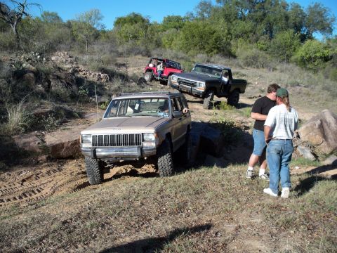 1996 Ford Bronco - Three off-road vehicles are parked on a dirt trail on a sunny day. A tan Jeep Cherokee is in the foreground, with a red Jeep Wrangler and a…