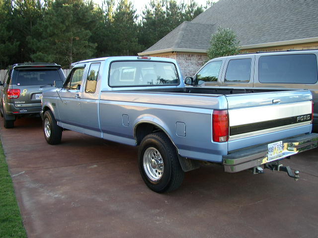 Light blue 1990s Ford F-series pickup truck, rear passenger side view, parked on concrete driveway.