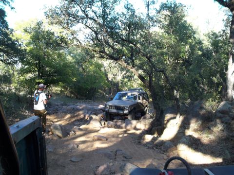 1996 Ford Bronco - A person wearing a backpack stands next to a brown Jeep Cherokee on a rocky, wooded trail. The Jeep is navigating the rough terrain, with s…