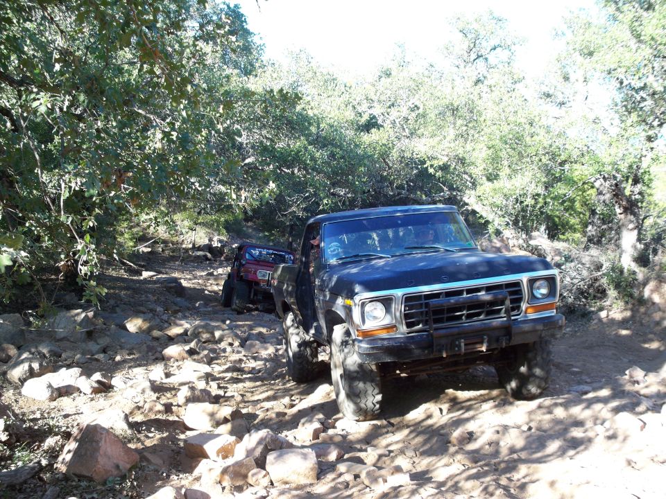 Black Ford pickup truck on a rocky off-road trail with trees.