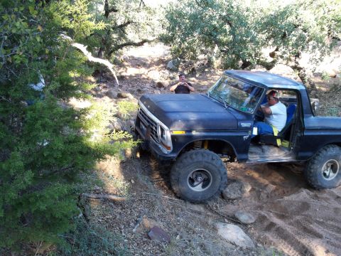 1996 Ford Bronco - A dark blue Ford Bronco is parked on a dirt trail surrounded by trees, with two men visible. One man is in the driver's seat, and another i…