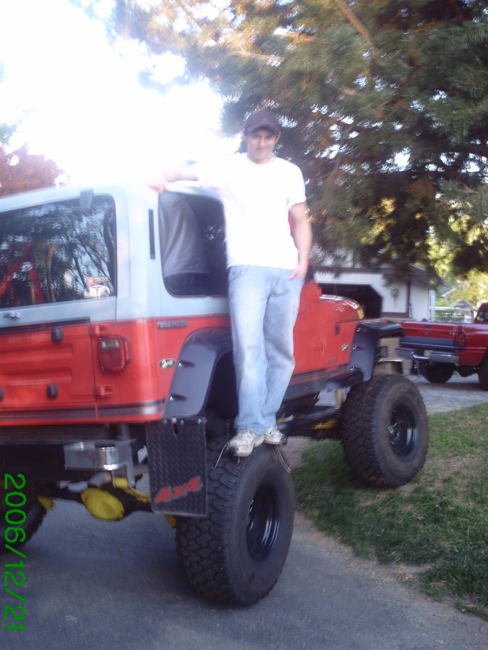 Man standing on a red and gray Jeep YJ with large off-road tires.