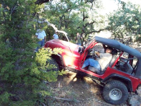 1996 Ford Bronco - A red Jeep Wrangler is navigating a rocky, wooded trail with two people visible outside the vehicle and one person driving. The Jeep is til…