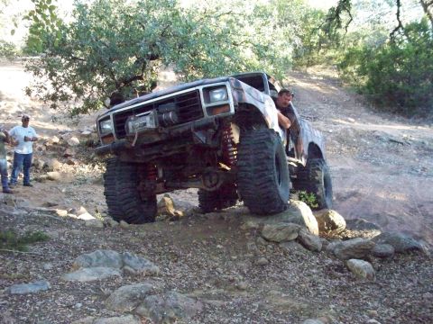 1996 Ford Bronco - A lifted, custom Ford Bronco is navigating a rocky, off-road trail with two people standing nearby. The vehicle features large, aggressive…
